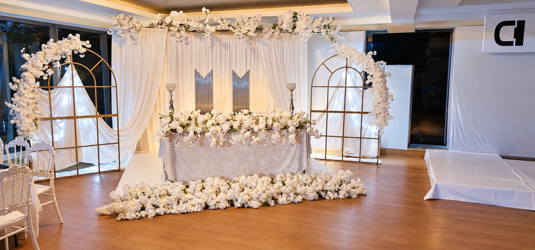 Brauttisch mit weißen Blumen, Vorhängen und goldenen Bögen im Arena Adlersaal